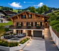 Two-story wooden house with a balcony, garage, and outdoor seating area with a sofa, coffee table, and dining set.