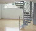 Empty room with wooden flooring and a modern spiral staircase leading to an upper level. The walls are white, and there is a large window on one side.