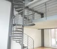 Modern interior with a sleek, black spiral staircase featuring a metal railing, leading to an upper level with a glass balcony overlooking the space.