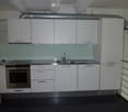 Modern kitchen with white cabinets, stainless steel sink, and built-in oven. Clean and minimalist design with a glass backsplash.