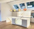 Modern kitchen with a large island, marble countertops, built-in cabinets, and pendant lights. Features a sleek fireplace on the left side and a double oven on the right.