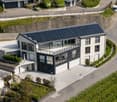 Modern two-story house with white exterior, solar panels on the roof, garage, and parking area.