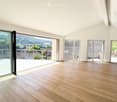 Bright, empty room with wooden flooring, large glass doors leading to a balcony with a scenic view of trees and a town.