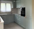 Modern kitchen with grey cabinets, a sink, and an oven, featuring tiled backsplash and tiled flooring.