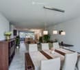 Modern dining and living area with a wooden dining table, white chairs, a sofa, coffee table, potted plants, and decorative vases.
