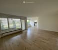 Empty room with wooden flooring, large window with blinds, and a sliding glass door leading to another room.