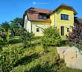 Two-story yellow house with red-tiled roof, multiple windows, and a front door, surrounded by a well-maintained garden with various plants and shrubs.