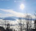 A serene mountain view with a clear blue sky, sun shining brightly, and a layer of clouds below the peaks.