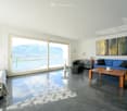 Bright living space with large windows offering a scenic mountain view, featuring a blue sofa, wooden coffee table, armchair, and a bed.
