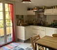 modern kitchen with white cabinets, black countertops, dining table, chairs, glass door leading to balcony, rugs, hanging lamp
