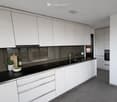 Modern kitchen with white cabinets, black countertops, and stainless steel sink. Includes a bowl, cutting board, bottle, and small plant on the counter.