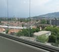 Balcony with a panoramic view of a cityscape, including houses, trees, and distant mountains.
