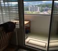 Balcony with a scenic city view, featuring a small table, a chair with a blanket, a radiator, and a trash bin.