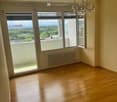 Empty room with wooden flooring, large windows offering a scenic view, and a chandelier hanging from the ceiling.
