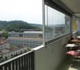 Balcony with a view of the city and surrounding hills, equipped with a small table, chairs, and an umbrella.