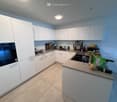 Modern kitchen with white cabinets, stainless steel appliances, and a central island with a countertop. The kitchen features a sink, microwave, and various kitchen items on the counter.