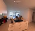 Modern kitchen with white cabinets, an island with an induction stove, and a dining area visible through an open doorway.