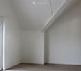 Empty room with light-colored wooden flooring and white walls, featuring a slanted ceiling and a small window on the left side.