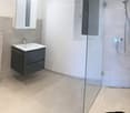 Modern bathroom with a toilet, sink, mirror, and a glass-enclosed shower area. The space features light-colored tiles and a sleek black cabinet under the sink.
