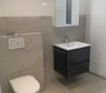Modern bathroom with beige marble tiles, white toilet, black sink cabinet, and illuminated mirror.