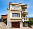 Two-story house with beige exterior, large windows, balconies, and a wooden garage door.