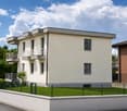 Two-story house with light beige exterior, multiple windows, balconies, and a fenced front yard.
