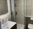 Modern bathroom with a white sink, chrome faucet, large mirror, glass-enclosed shower, and a toilet. Shelves inside the shower hold toiletries.