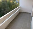 Balcony with tiled floor, white railing, and view of greenery and trees.