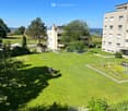 Well-maintained lawn with trees, shrubs, and a playground with swings and a slide, surrounded by residential buildings.
