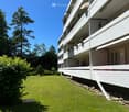 A multi-story residential building with balconies, surrounded by a well-maintained lawn and trees.