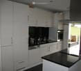 Modern kitchen with white cabinets, black countertops, stainless steel appliances, and a large window overlooking a green field.