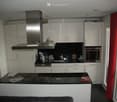 Modern kitchen with white cabinets, stainless steel appliances, black countertop, and a small seating area with a sofa and table.