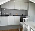 Modern kitchen with white cabinets, stainless steel appliances, a sink, a mixer, and a dining area with a white table and chairs.