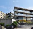 Modern multi-story residential building with balconies, glass railings, and a raised ground floor entrance.
