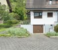 Two-story house with a garage, surrounded by greenery and a well-maintained garden. The house features a tiled roof, white walls, and multiple windows with blinds.