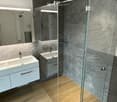 Modern bathroom with two sinks, a large mirror, a glass-enclosed shower, and wooden flooring.