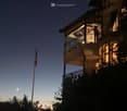 A multi-story building with illuminated balconies and a flagpole visible against a twilight sky.