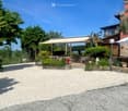 Outdoor seating area with tables, chairs, and an umbrella, surrounded by greenery and a gravel driveway.