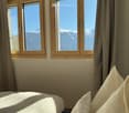 Bright bedroom with large windows offering a scenic mountain view, featuring a neatly made bed with pillows.