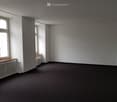 Empty room with white walls, black floor, two windows, wooden window sills, and a radiator.