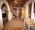 Cozy hallway with wooden staircase, tiled floor, and decorative items including a small table with candles, a cat, and a red sofa visible in the background.