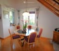 Dining room with wooden floor, round wooden dining table, six chairs, flower pot, cabinet, and picture frame on the wall.