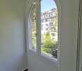 A narrow hallway with arched windows offering a view of a residential area and greenery outside.