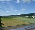Balcony overlooking a rural landscape with fields, a town, and distant hills under a partly cloudy sky.
