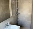 Modern bathroom with a white sink, chrome faucet, a cup on the sink, and a showerhead with a flexible hose mounted on a tiled wall.