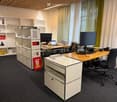 Modern office space with a wooden desk, ergonomic chair, dual monitors, laptop, keyboard, mouse, books, and storage units.