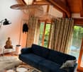A cozy living room with a dark blue sofa, wooden tables, a fur rug, and large windows with curtains. The room features a unique hanging lamp and a decorative statue on a side table.