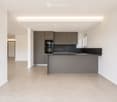Modern, minimalist kitchen with grey cabinets, a central island, and a sleek black countertop. The space features recessed lighting and a tiled floor.