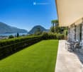 Well-maintained garden with artificial grass, a small patio area with a table and chairs, overlooking a scenic lake and mountain view.