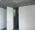 Modern, minimalist hallway with concrete ceiling and floor, white walls, and an open staircase leading upwards.